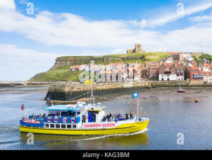 Whitby, North Yorkshire. GROSSBRITANNIEN. Blick über den Hafeneingang zur Kirche St. Mary`s mit Touristenboot im Vordergrund. Stockfoto